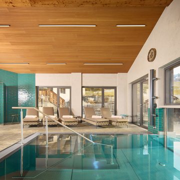 Ferienwohnung im Zillertal mit Panoramablick Innenpool mit Liegestühlen und Blick auf die Berge durch große Fenster