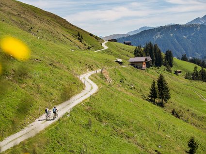 Dein Apartment im Zillertal in bester Lage Zwei Radfahrer auf einem bergigen Wanderweg mit Hütten und Bergen im Hintergrund