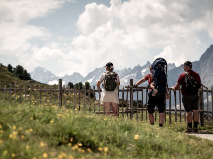 Sommer bei Zell am Ziller: wandern, abschalten und genießen Drei Wanderer mit Rucksäcken blicken auf Berglandschaft hinter Holzzaun