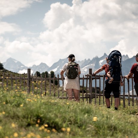 Sommer im Zillertal für die ganze Familie Drei Wanderer mit Rucksäcken blicken auf Berglandschaft hinter Holzzaun